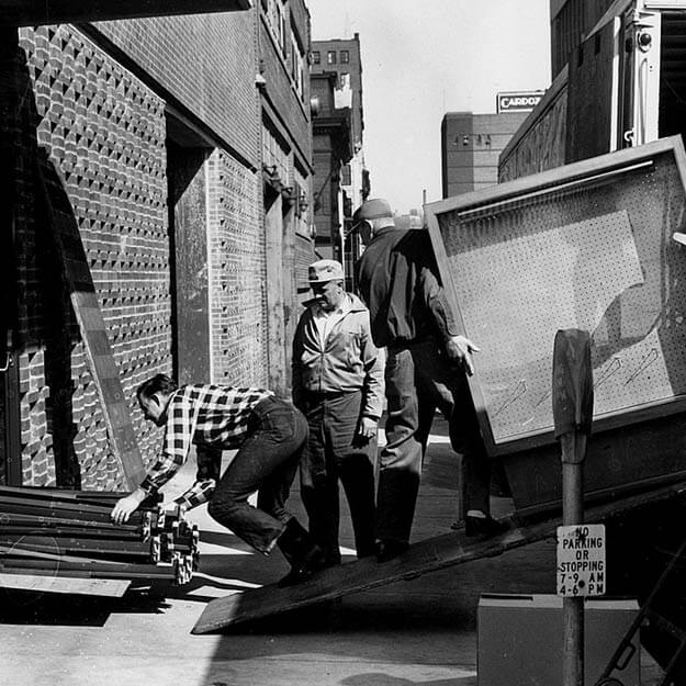 1960s black and white photo of movers moving furniture into a building