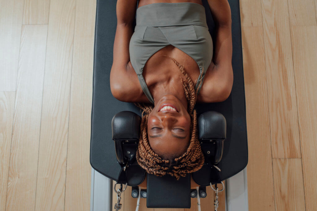 From above photo of pretty African smiling woman in sportswear lying on pilates reformer.