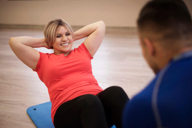 Personal trainer holding the feet of a mature woman doing crunches