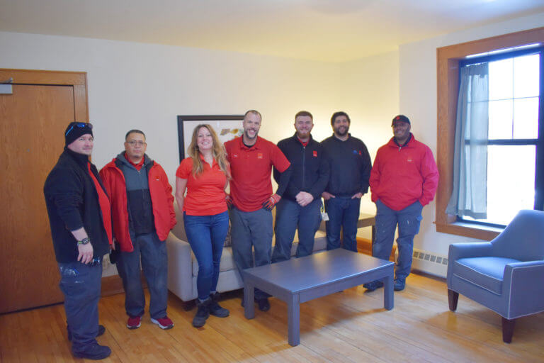CORT furniture volunteer team standing in the living room of the apartment unit that they painted and furnished