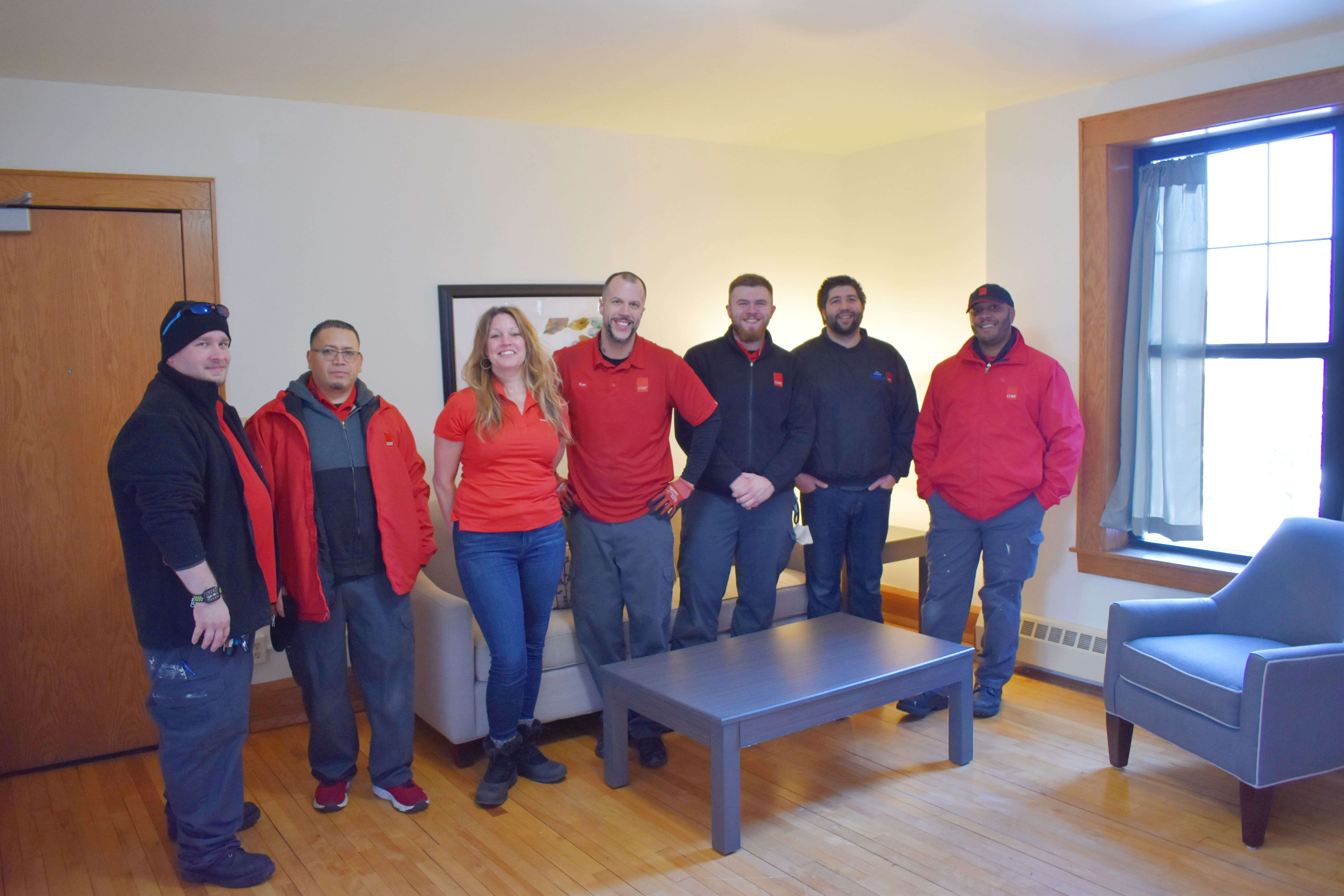 CORT furniture volunteer team standing in the living room of the apartment unit that they painted and furnished