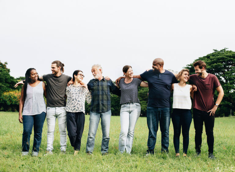 multi-racial group of people hugging each other in park