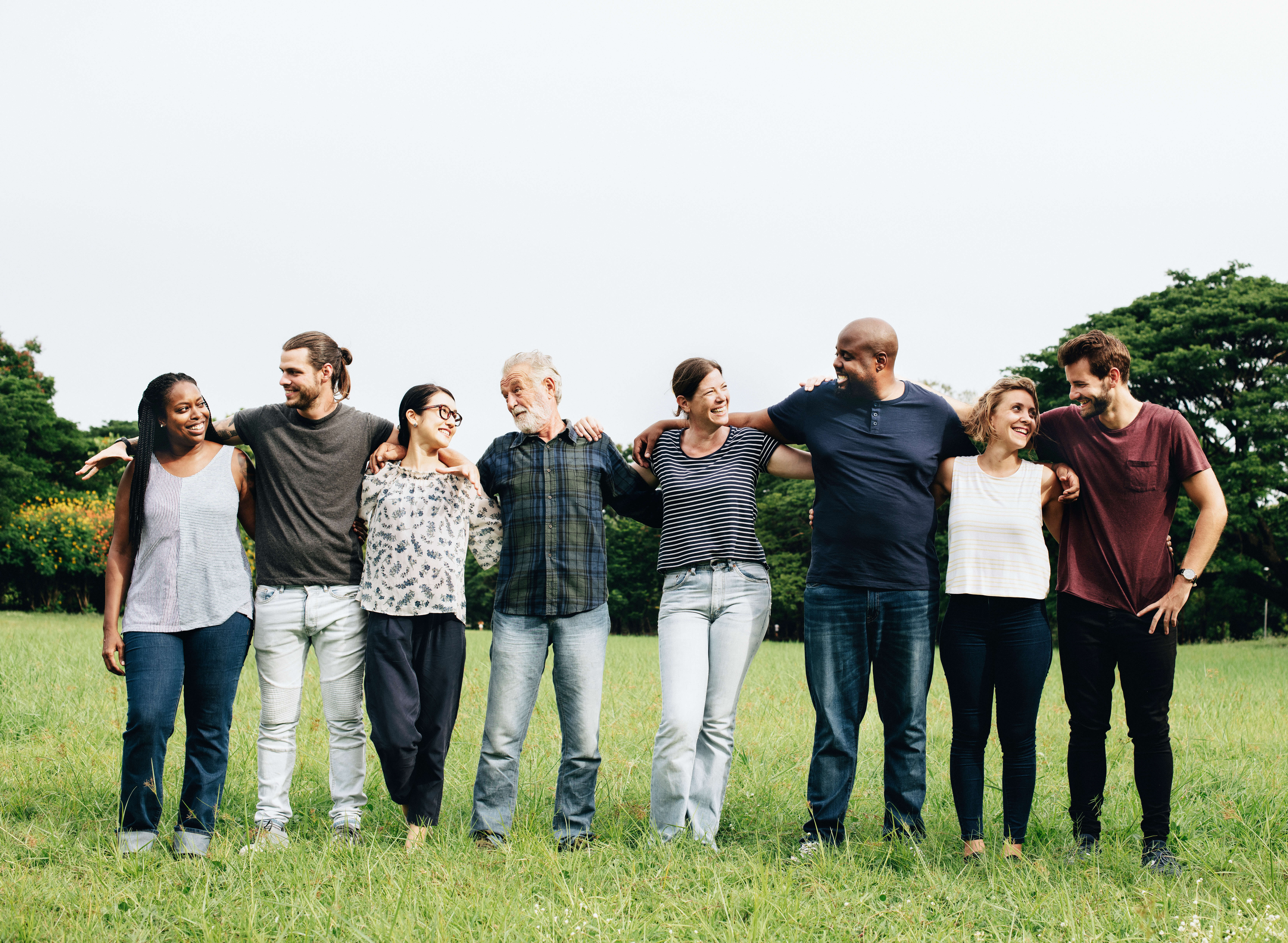 multi-racial group of people hugging each other in park