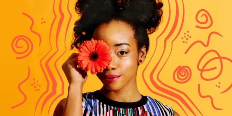 Young African American woman smiling and while holding an orange flower in front of her face. The background is a yellow gradient with orange doodles.