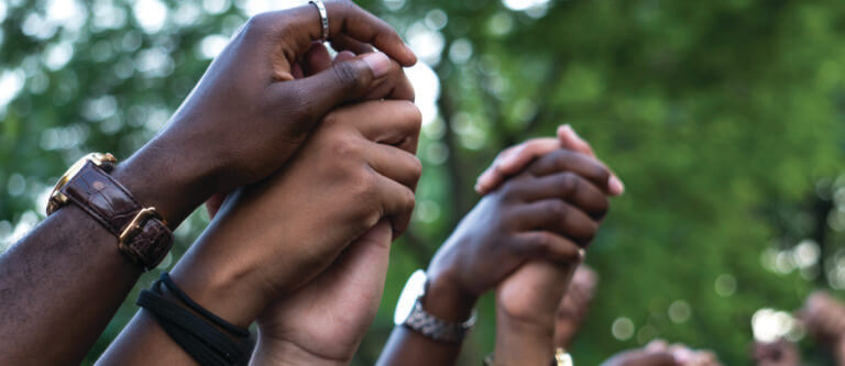 multiracial hands clasped together overhead in protest