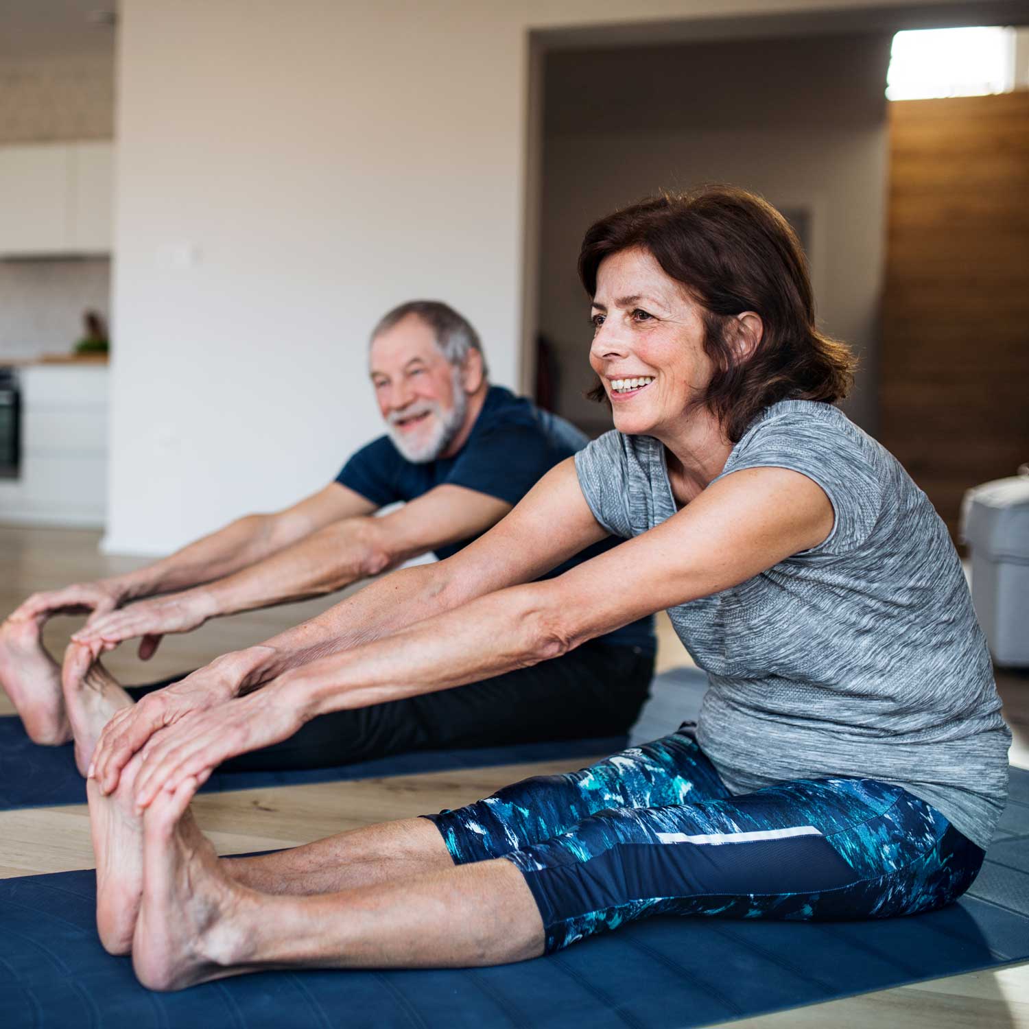 mature white couple in sitting forward fold pose at home workout