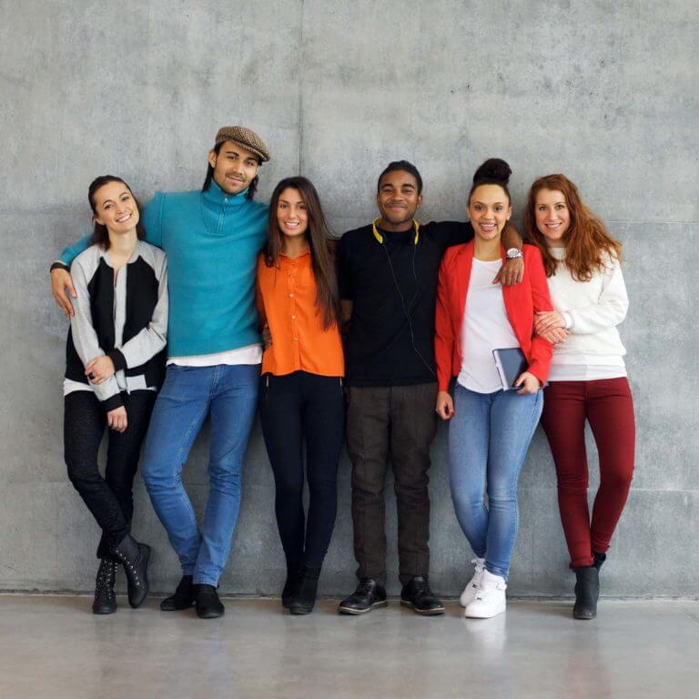 group of multiethnic teens hugging each other while leaning against wall