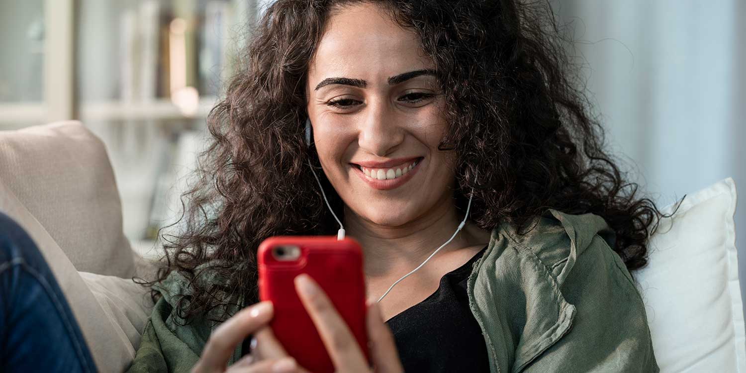 Teen with curly hair smiling while looking at phone - appears to be engaged in a video chat