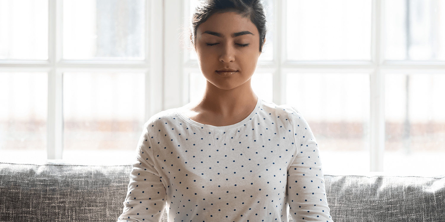 Peaceful Indian woman meditating on couch