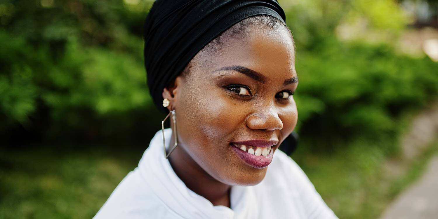 Close up portrait of african muslim girl in black hijab, white sweatshirt sitting outdoor.