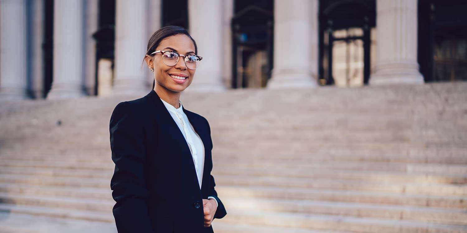 African American woman smiling at camera, wearing formal suit in front of judicial steps