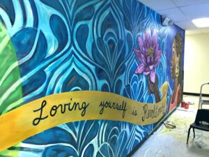 Mural on wall at YWCA St. Paul facility reading "Loving yourself is revolutionary" with bright colors and a woman holding a purple flower